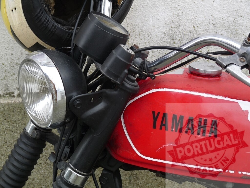 Close-up of red Yamaha motorcycle with helmet hanging on handlebar | Red Yamaha motorcycle parked against a wall, featuring a helmet resting on the handlebar - Realisiert mit Pictrs.com