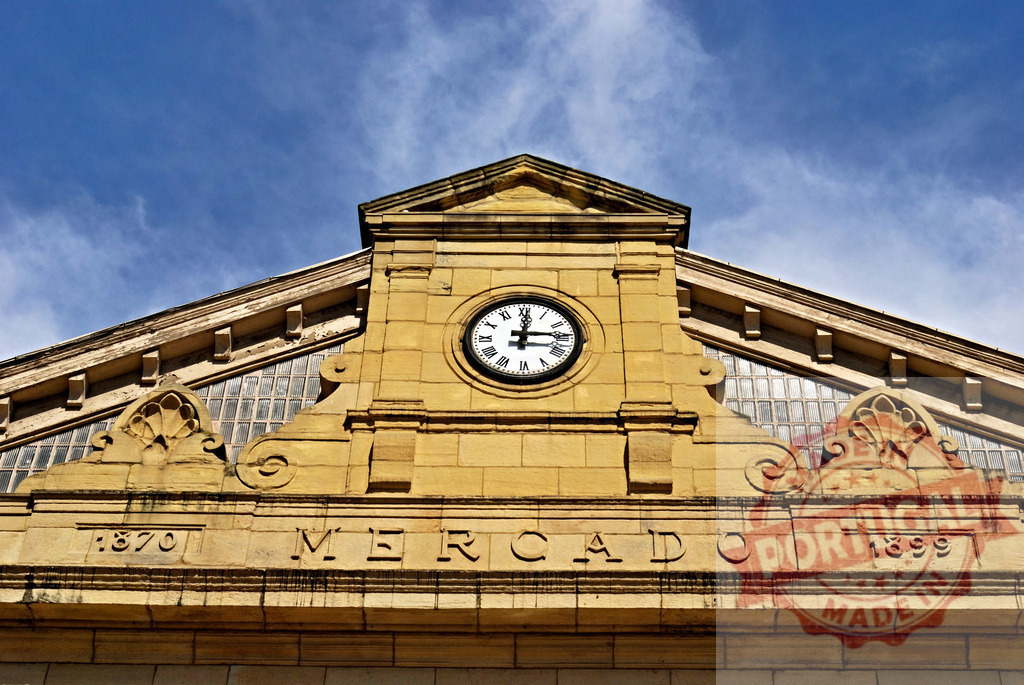Mercado building facade displaying clock and historical dates. Spain - Cantabria | Mercado building facade architectural details with clock, years, and decorative elements under blue sky - Realisiert mit Pictrs.com