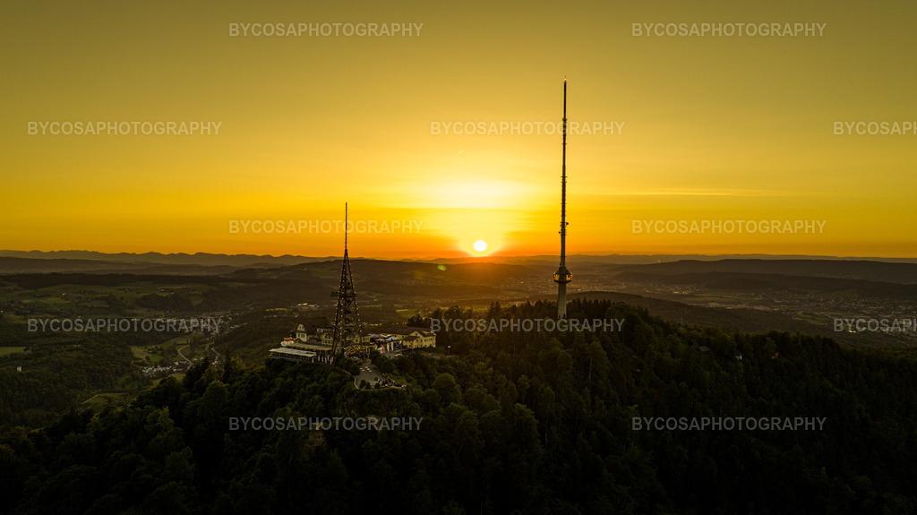 Uetliberg Sunset _ Golden Skyline | Ein atemberaubender Luftblick auf den Uetliberg, eingefangen in der perfekten goldenen Stunde. Die Sonne versinkt direkt hinter den fernen Hügeln und taucht die gesamte Landschaft in warme Goldtöne, während sich der ikonische Aussichtsturm und der Sendemast des Uetlibergs als Silhouetten gegen den leuchtenden Himmel abzeichnen.Dieser minimalistische, elegante FineArt-Druck verleiht jedem Raum Wärme, Ruhe und ein modernes Ambiente – ideal für alle, die Zürich und Sonnenuntergänge lieben. - Realisiert mit Pictrs.com