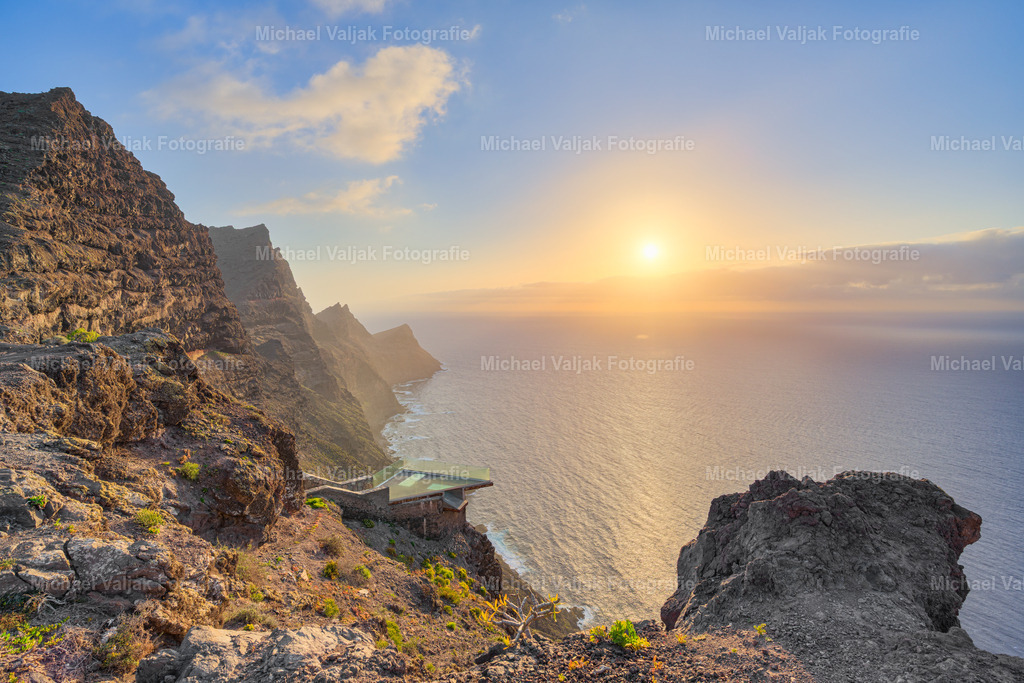 Mirador del Balcón auf Gran Canaria | Ein Bild vom Mirador del Balcón bei Sonnenuntergang ist eine Hommage an die wilde Schönheit der Westküste Gran Canarias. Die steilen Klippen, die sich dramatisch ins Meer stürzen, werden von warmen, goldenen Lichtstrahlen umhüllt, während die Sonne langsam hinter dem Horizont verschwindet. Die Szenerie ist atemberaubend – der Atlantik erstreckt sich in endloser Weite, und die schroffen Felsen bilden eine fast surreal wirkende Kulisse.Dieses magische Zusammenspiel aus Licht und Natur macht den Mirador del Balcón zu einem der spektakulärsten Aussichtspunkte der Insel. Die „Drachenrücken“-Formation der Küstenlinie verleiht dem Panorama eine mystische Note und lässt die Landschaft noch eindrucksvoller wirken. - Realisiert mit Pictrs.com