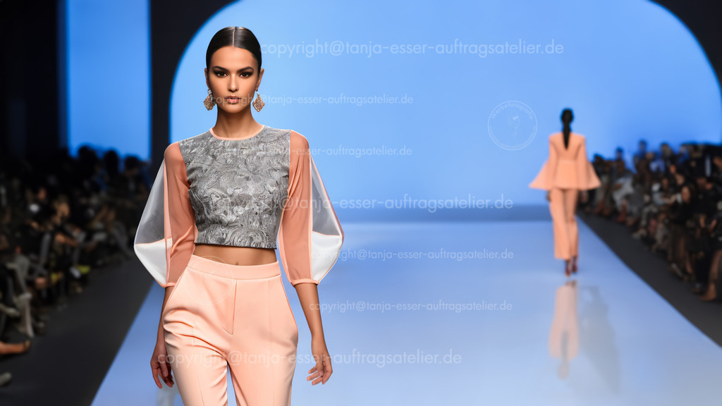 KI macht Mode 2 E | Fotorealistiche KI Modenschau. Das von KI entworfene Outfit greift aktuelle Modethemen wie Transparenz, bauchfrei, hohe Taille und die Farbe Pfirsich auf. Zuschauer und Pressevertreter sitzen im unscharfen Hintergrund.