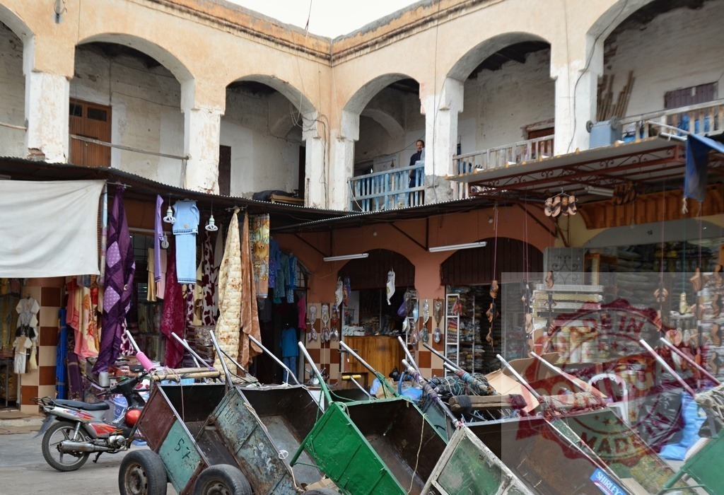 Hand carts parked outside market stalls in Marrakech souk | Market carts standing in front of shops selling textiles and goods in North Africa - Realized with Pictrs.com
