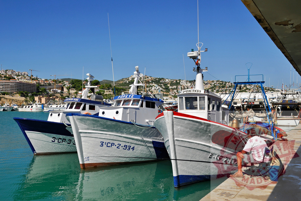 Fishing boats moored in Peñíscola harbor, Spain. Spain - Castellon | Fisherman resting by trawler boats moored in a bustling Peñíscola port under a blue sky - Realisiert mit Pictrs.com