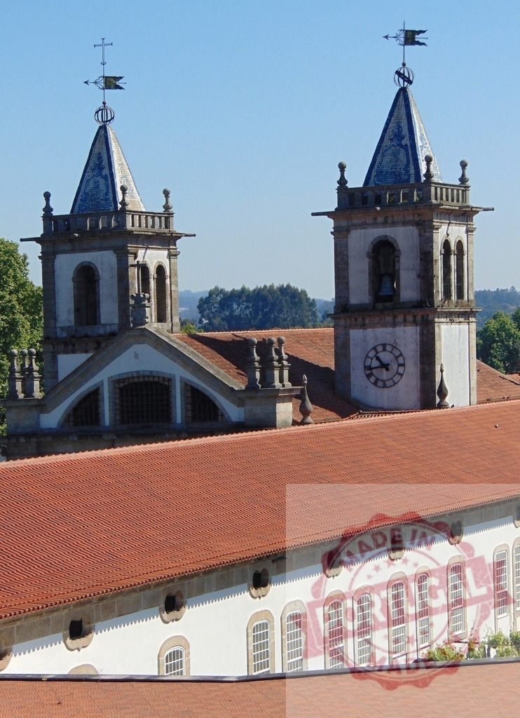 Historic church towers with clock and tiled roofs. Region Norte - Portugal | Historic church towers with a clock, bell, and traditional tiled roofs under a blue sky - Realized with Pictrs.com