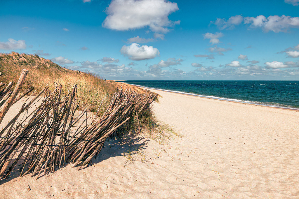 Dünenlandschaft am Strand in Sylt-Ellenbogen-Holzzaun-Sand | Landschaft: Dieses Bild zeigt den Ellenbogen auf der Nordseeinsel Sylt, gekennzeichnet durch seine weitläufigen Sandstrände, Dünenlandschaften und typischen Holzzäune.Geografie: Der Ellenbogen ist der nördlichste Punkt Deutschlands und befindet sich in der Nähe des Ortes List.Aktivitäten: Das Gebiet ist bekannt für seine Natur, eignet sich gut für Strandspaziergänge und Hunde sind an langen Leinen erlaubt. - Realisiert mit Pictrs.com