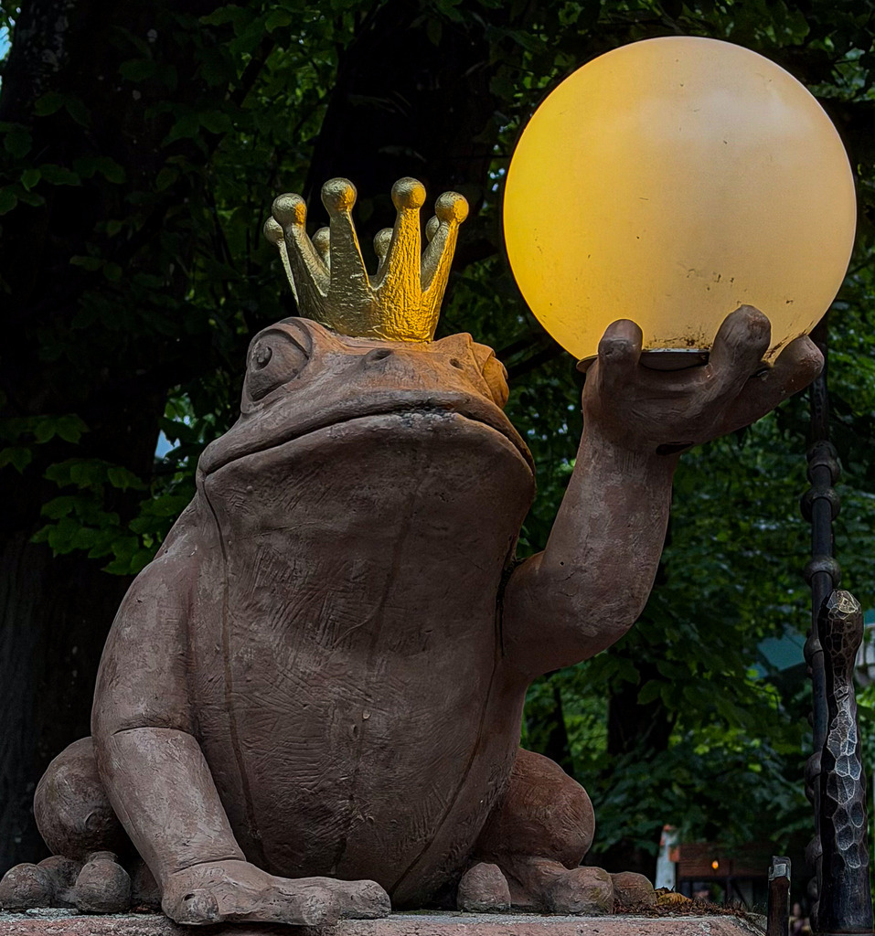 Der Froschkönig – Mystische Märchen Fotokunst Wandbild | Magische und detailreiche Fotokunst: Dieses High-End Wandbild fängt den legendären Froschkönig mit seiner goldenen Krone und einer warm leuchtenden Kugel ein. Der faszinierende Kontrast zwischen der rauen, haptischen Steinstruktur der Skulptur und dem mystischen Glanz der Kugel verleiht dem Motiv eine zeitlose, märchenhafte Atmosphäre. Ein exklusiver Blickfang in Galeriequalität auf Acrylglas oder Leinwand – perfekt für Wohnräume, Bibliotheken oder als kreative Dekoration. - Realisiert mit Pictrs.com