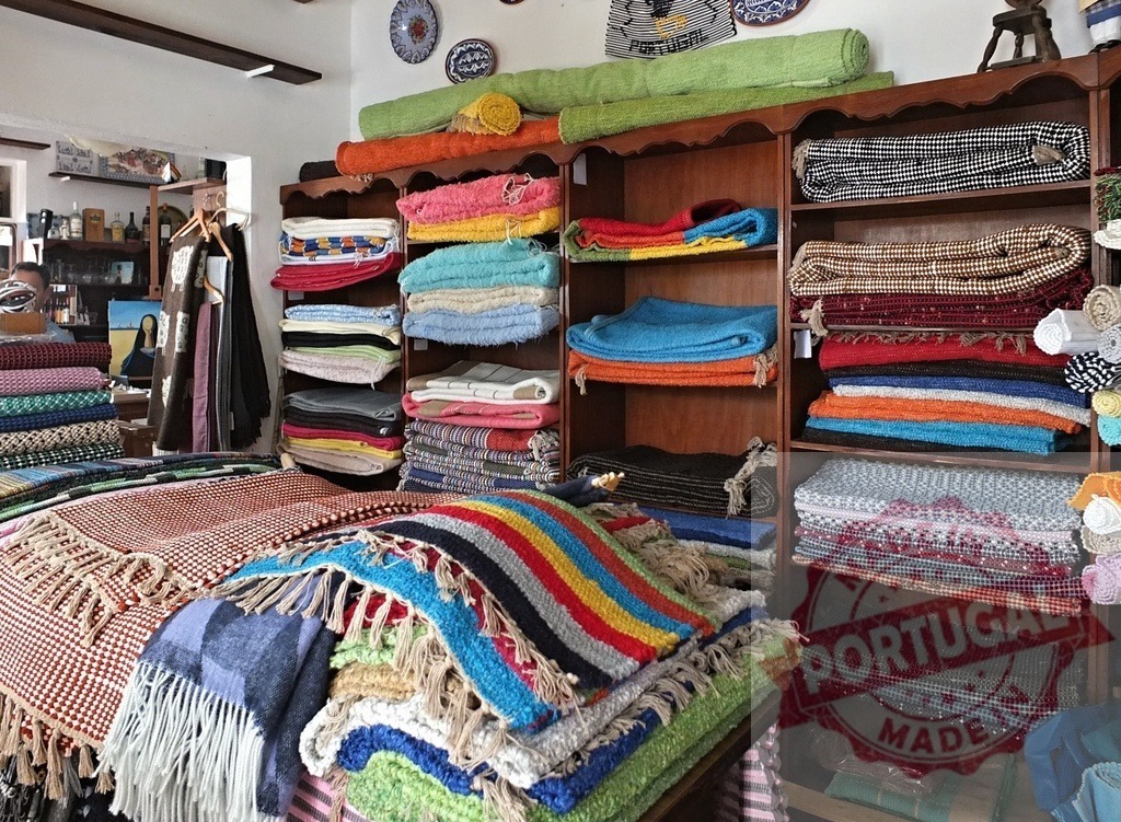 Colorful handmade Portuguese textiles and blankets in shop | Displaying a vibrant collection of traditional handmade Portuguese textiles and crafts for sale - Realisiert mit Pictrs.com