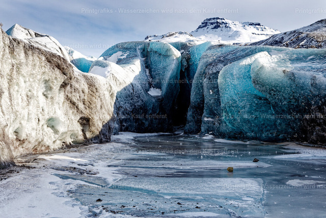 Blaues Eis am Gletscher in Island | Nahaufnahme einer eisigen Gletscherlandschaft in Island mit blau schimmernden Eiswänden, gefrorener Wasserfläche und schneebedeckten Bergen im Hintergrund. Die klaren Strukturen und kalten Farbtöne vermitteln die stille, raue Schönheit der arktischen Natur. - Realisiert mit Pictrs.com