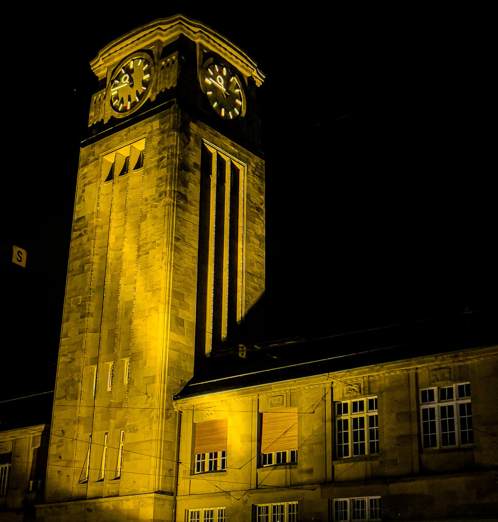 Wandbild Kunstdruck Poster – Badischer Bahnhof Basel bei Nacht | Ein atmosphärisches Meisterwerk der urbanen Nachtfotografie, das die zeitlose Eleganz der Schweiz direkt in deine Räume bringt. Diese faszinierende Aufnahme fängt den markanten Uhrturm des Badischen Bahnhofs in Basel in den späten Stunden perfekt ein. Die historische Architektur erstrahlt in einem warmen, goldenen Licht, das sich in spektakulärem Kontrast gegen den tiefen, mystischen Nachthimmel absetzt. Die feinen Linien des Bauwerks und die nächtliche, urbane Ruhe verleihen dem Motiv eine edle, ehrfürchtige Dynamik.Dieses exklusive Kunstwerk ist der perfekte, stilvolle Blickfang für ein modernes Wohnzimmer, das repräsentative Büro, ein urbanes Loft oder für eine einladende Atmosphäre im Flur und Konferenzraum – ganz besonders für Liebhaber der Stadt Basel und klassischer Architektur.Um das goldene Leuchten und die tiefen Kontraste dieser Nachtaufnahme mit maximaler Brillanz an deine Wand zu bringen, empfehle ich unsere Premium-Materialien: Erlebe kinoreife Tiefe und Leuchtkraft auf edlem Acrylglas, hochmoderne Eleganz auf robustem Alu-Dibond oder klassischen Galerie-Charakter auf einer matten Leinwand. Hol dir dieses Stück Basler Geschichte direkt nach Hause! - Realisiert mit Pictrs.com