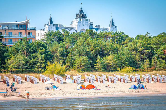 2026-08-05_11-07-43_230 | Ein belebter Strand mit Sonnenschirmen und einem prächtigen Gebäude umringt von Wald, Zinnowitz, Usedom, Mecklenburg-Vorpommern, Deutschland - Realisiert mit Pictrs.com