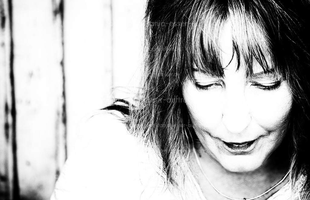 Authentische Frau D | Monochromes Portrait einer Frau in den 40ern. Sie lächelt und senkt den Blick. Starke Kontraste.