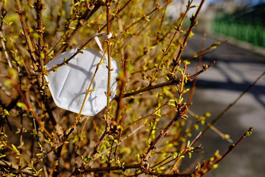 FFP2 Maske im blühenden Strauch neben dem Gehsteig | Wien, Austria - March 12, 2021: Massnahmen zur Einschränkung von COVID-19; FFP2 Maske im blühenden Strauch neben dem Gehsteig. - Realisiert mit Pictrs.com