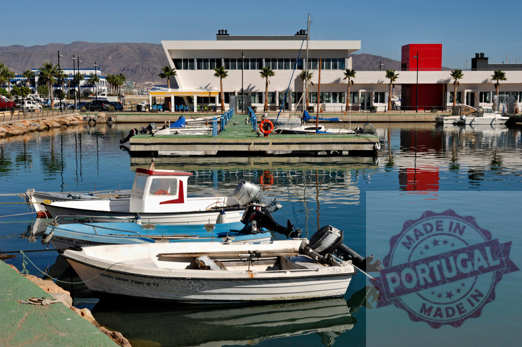 Fishing boats reflecting in a sunny marina harbor | Small boats moored in a calm harbor with modern buildings and mountains reflecting on water - Realisiert mit Pictrs.com