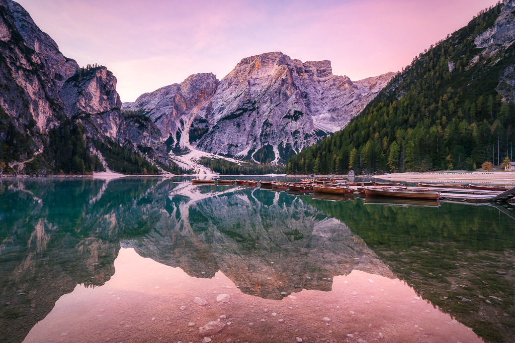 Stille am Morgen – Sonnenaufgang am Pragser Wildsee | Ein klarer Herbstmorgen am Pragser Wildsee: Die Spiegelung der Berge im glatten Wasser und das zarte Licht der aufgehenden Sonne verleihen der Szene eine fast surreale Ruhe. Ein perfekter Start in den Tag. - Realisiert mit Pictrs.com