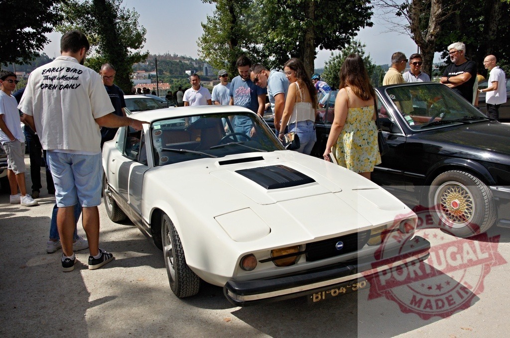 Enthusiasts admiring classic Saab Sonett III at outdoor car show | Car enthusiasts gathering and looking at a vintage white Saab Sonett III sports car outdoors - Realisiert mit Pictrs.com