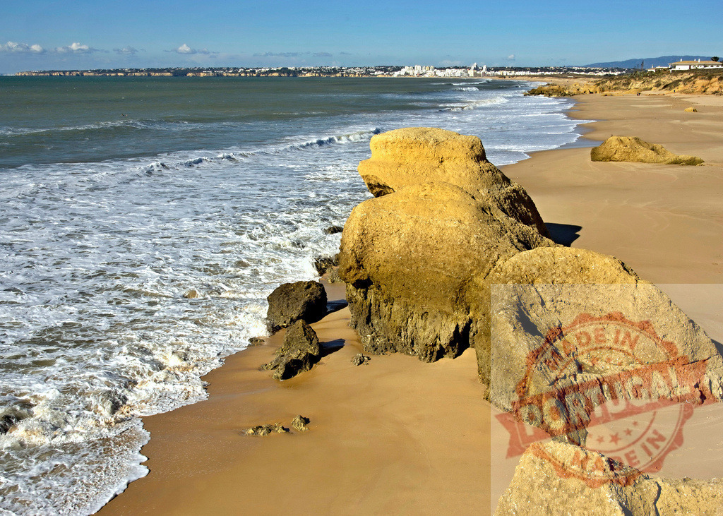 Algarve Atlantic coastline with dramatic sandstone rock formations | Waves washing over the golden sand beach with a distant coastal town - Realized with Pictrs.com