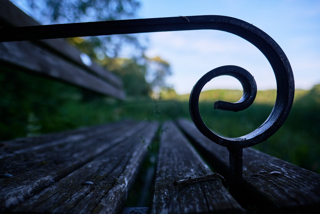 Alte Holzbank in der Wiese | Burgenland, Austria - June 12, 2020: Alte Holzbank in der Wiese mit Spiralenförmiger Armstütze aus Metall. - Realisiert mit Pictrs.com