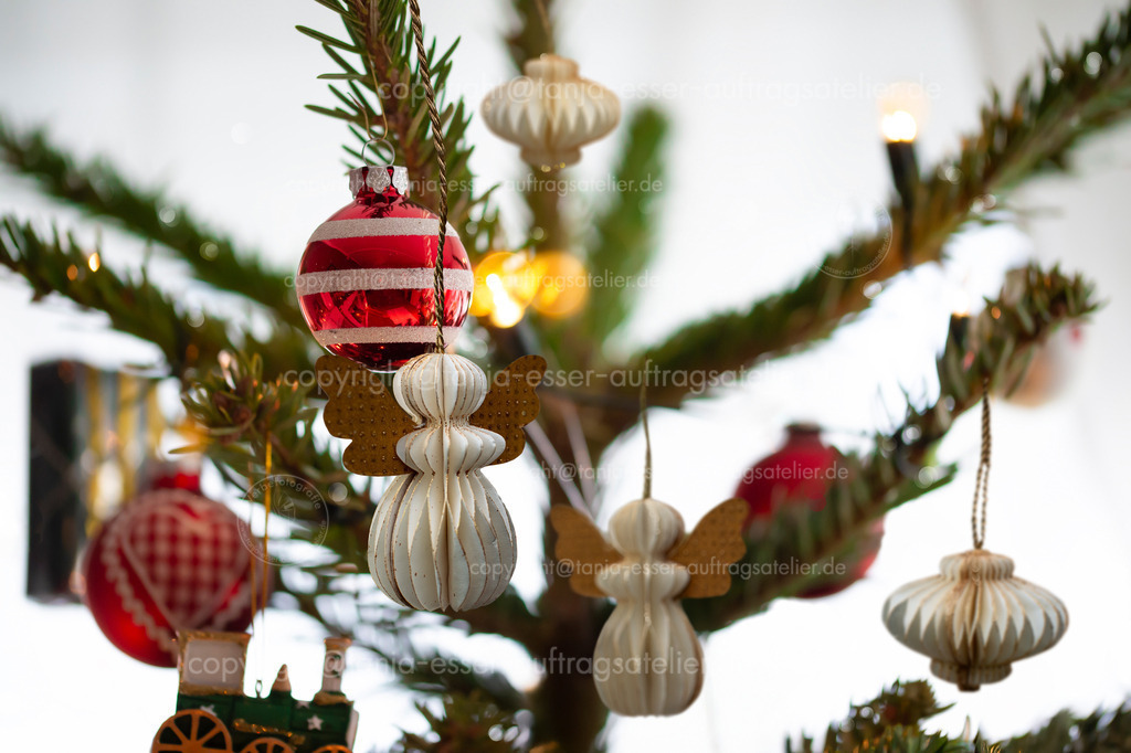 Weihnachtsbaum Wabenhaenger nah D | Geschmückter Weihnachtsbaum, echte Nordmanntanne. Makrofotografie zeigt verschiedene Anhänger im neuen Design mit Weihnachtsbaum Ornamenten aus Wabenpapier.  Rot weiß. Papier Waben Engel.