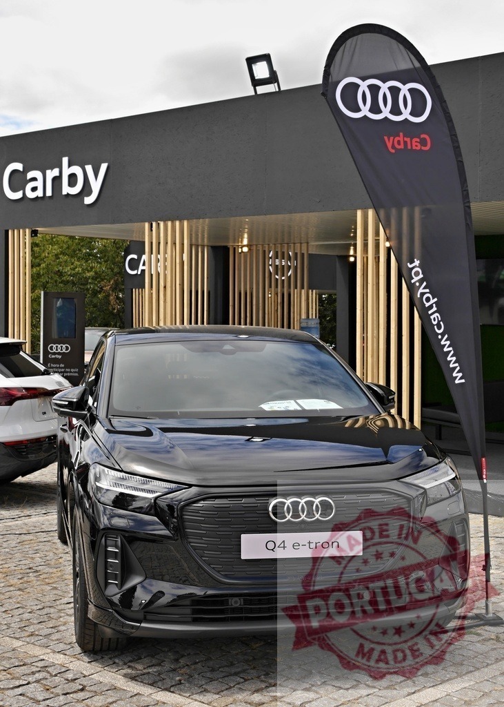 Audi Q4 e-tron electric SUV at Carby dealership event | Audi Q4 e-tron parked in front of Carby dealership with promotional flag - Realized with Pictrs.com