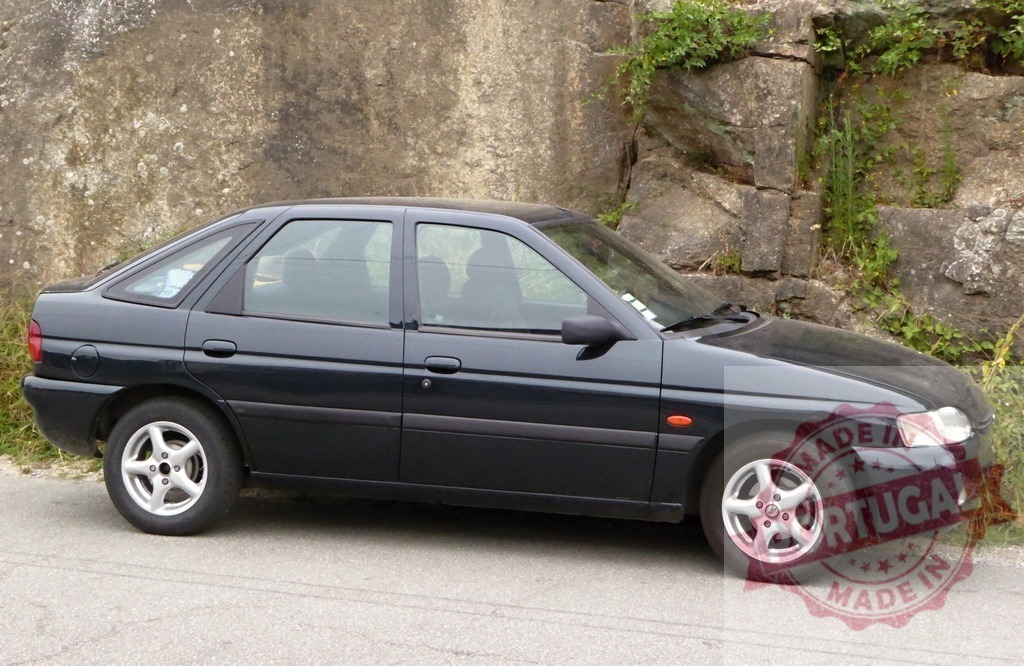 Ford Escort Generation 6 black hatchback parked by rock wall | Black Ford Escort Mark VI hatchback parked on a paved road next to a stone wall - Realized with Pictrs.com
