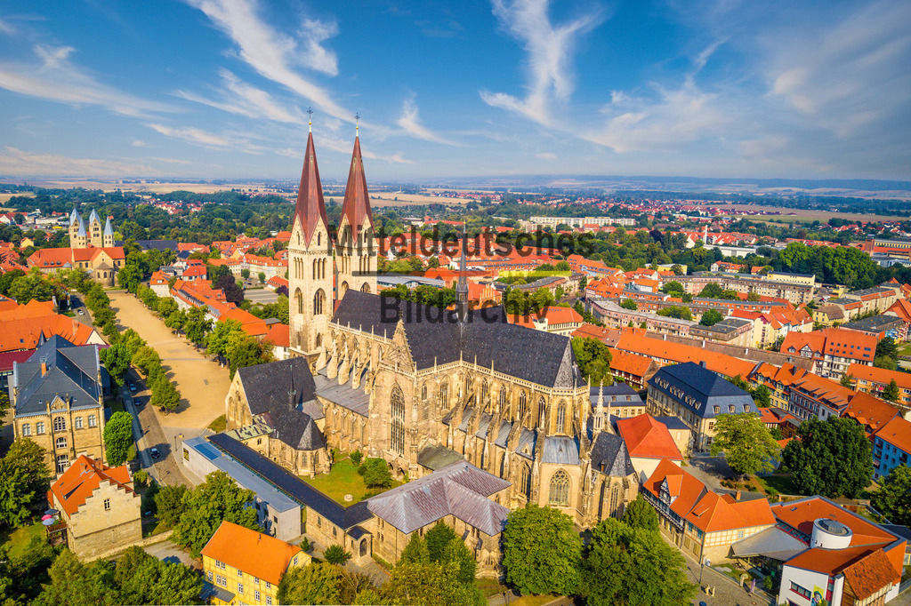 Dom Halberstadt Luftbild LU-0022 | Dieses Luftbild zeigt den Dom St. Stephanus und St. Sixtus in Halberstadt in Sachsen-Anhalt an einem eindrucksvollen Sommertag. Die mächtige Kathedrale zählt zu den bedeutendsten gotischen Bauwerken Deutschlands und prägt mit ihren markanten Türmen seit Jahrhunderten die Silhouette der historischen Bischofsstadt. Aus der Vogelperspektive werden die beeindruckenden Ausmaße des Doms und seine zentrale Lage innerhalb der Altstadt besonders deutlich sichtbar.Besonders faszinierend wirkt die außergewöhnliche Wolkenformation über der Stadt und verleihen der Aufnahme eine eindrucksvolle Dynamik. Das Zusammenspiel aus Sonnenlicht, Wolkenschatten und der monumentalen Architektur des Doms schafft eine außergewöhnliche Atmosphäre und lenkt den Blick auf eines der bedeutendsten Kulturdenkmale Sachsen-Anhalts.Halberstadt blickt auf eine mehr als tausendjährige Geschichte zurück und war über viele Jahrhunderte ein bedeutendes geistliches Zentrum Mitteldeutschlands. Der Dom mit seinem weltberühmten Domschatz gehört zu den wichtigsten Sehenswürdigkeiten der Region und zieht Besucher aus aller Welt an.Dieses Luftbild verbindet historische Architektur, Stadtgeschichte und eine spektakuläre Wetterstimmung zu einem eindrucksvollen Blick auf die Domstadt Halberstadt in Sachsen-Anhalt. - Realisiert mit Pictrs.com