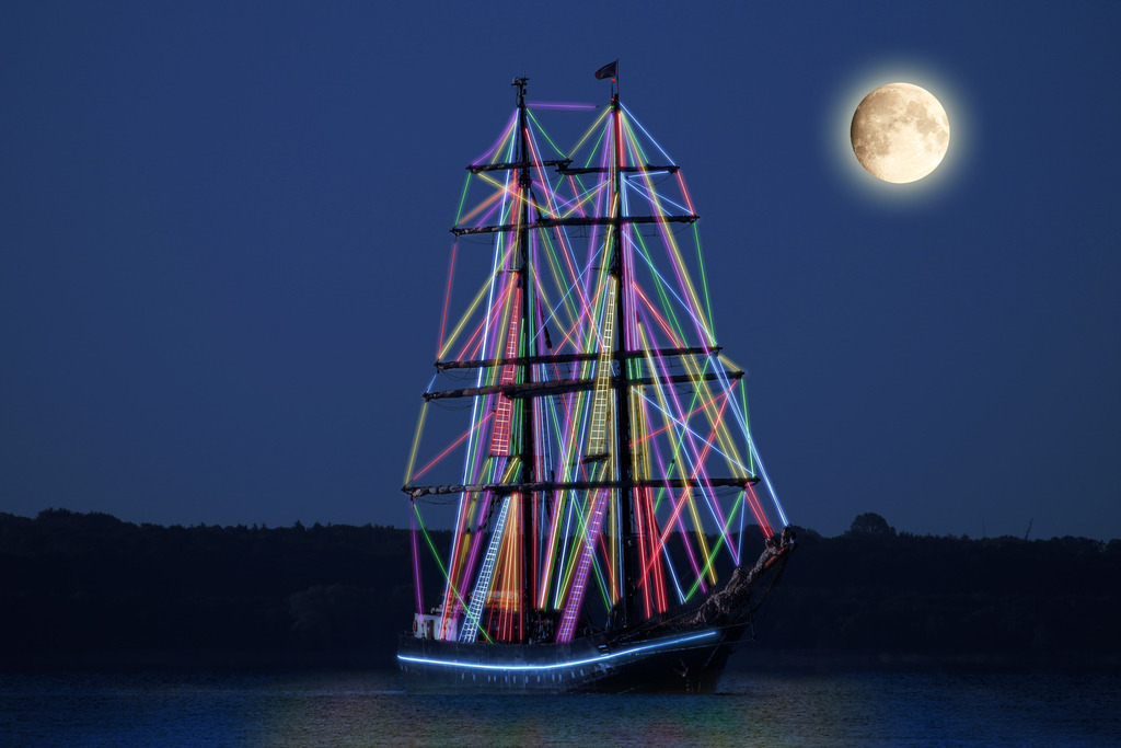 Photoart: Traditionssegler mit Neontakelage | Dieses Wandbild im Querformat zeigt die künstlerische Interpretation eines Traditionsseglers mit Neontakelage. Die leuchtenden Seile spiegeln sich im Wasser. Am Himmel befindet sich der Vollmond. Dieses Wandbild bietet eine Besonderheit. Es gehört sowohl zur Photoartserie Moonlight in der weitere maritime Orte im Mondlicht gezeigt werden als auch zur Photoartserie: Maritimes Neonlicht.  - Realisiert mit Pictrs.com