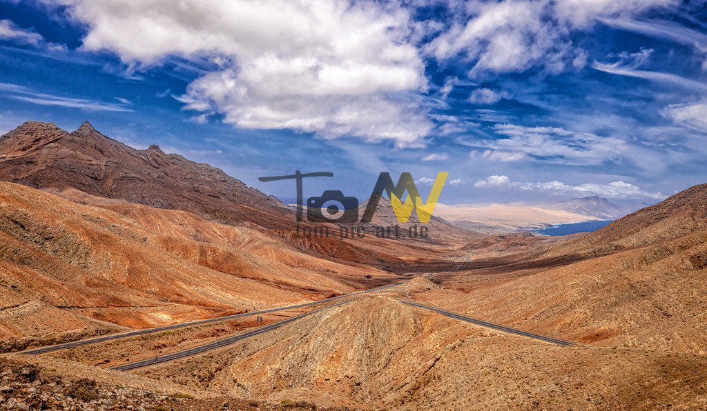Blick über die sanften Hügel--Landschaft von Fuerteventura | Viele Straßen wurden zum Zeitpunkt der Aufnahme neu geteert. Schlängeln sich kurvenreich durch die sanften Hügelketten Fuerteventuras. Blauer Himmel, blick soweit das Auge reicht... - Realisiert mit Pictrs.com