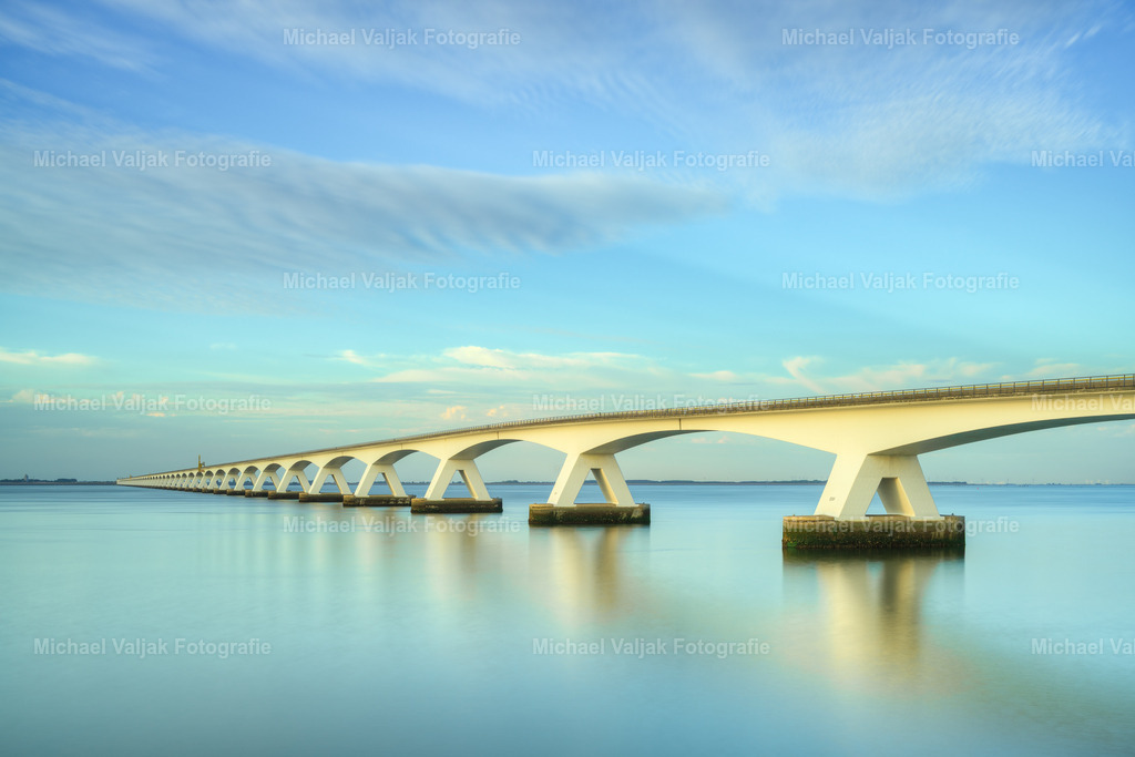 Zeelandbrücke – Langzeitbelichtung im Abendlicht | Im sanften Licht des frühen Abends zieht sich die imposante Zeelandbrücke weit über das Wasser. Die lange Reihe ihrer Pfeiler bildet eine kraftvolle grafische Linie, während die Langzeitbelichtung die Bewegung des Wassers in weiche, fließende Strukturen verwandelt.Das warme Abendlicht und die ruhige Wirkung der Langzeitbelichtung verleihen der Szenerie eine besondere Tiefe und zeitlose Atmosphäre. Die Zeelandbrücke erscheint dabei nicht nur als beeindruckendes Bauwerk, sondern als harmonische Verbindung zwischen Himmel, Wasser und Landschaft.Ein stimmungsvolles Landschaftsfoto aus Zeeland, Niederlande, das die besondere Schönheit der niederländischen Küste mit der minimalistischen Ästhetik einer Langzeitbelichtung verbindet. - Realisiert mit Pictrs.com