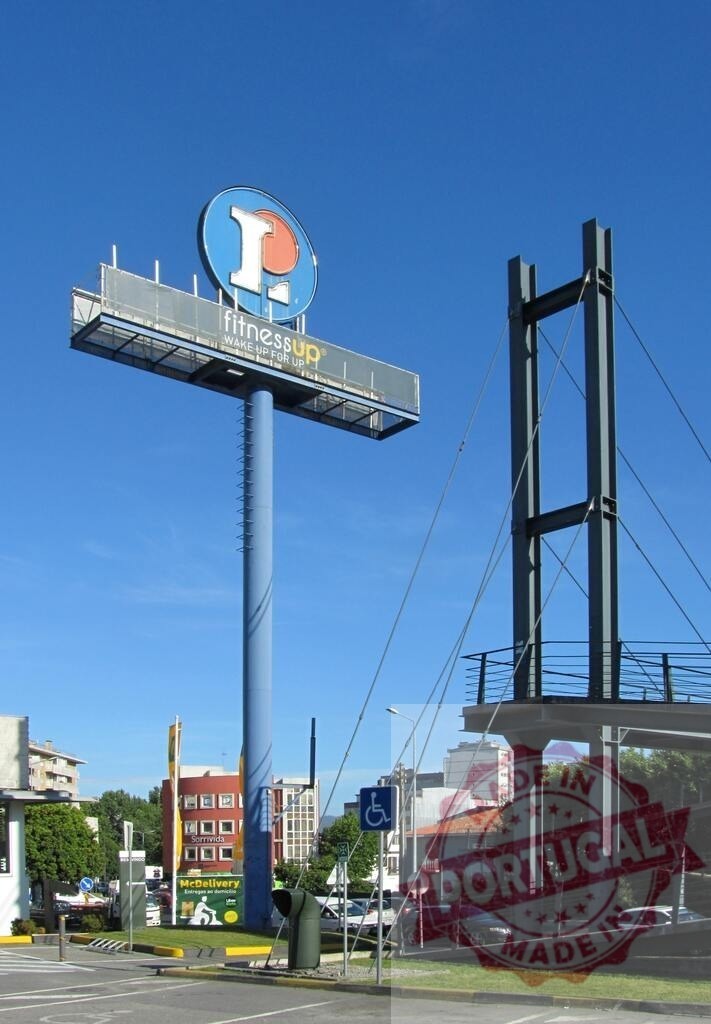 Tall commercial sign pole with shopping mall logo | Shopping center entrance with a large sign pole and pedestrian bridge - Realisiert mit Pictrs.com