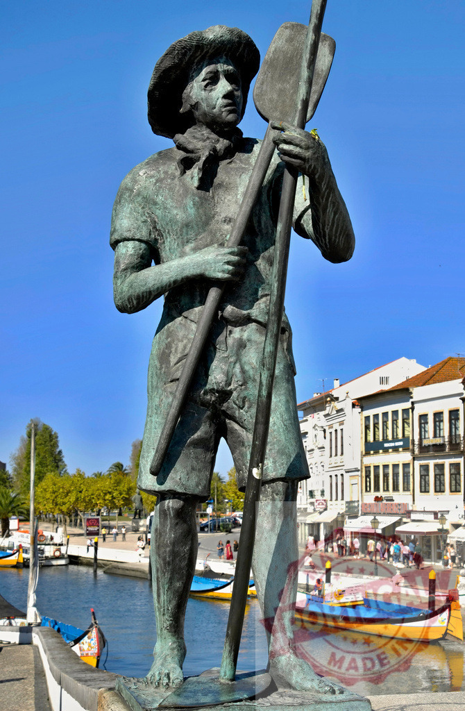 Statue representing moliceiro gondolier in Aveiro canal | Bronze statue depicting a moliceiro boatman in Aveiro, with traditional boats on the canal - Realisiert mit Pictrs.com