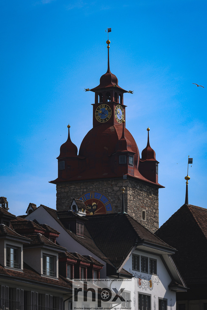 Rathausturm Luzern | Tradition. Wahrzeichen. Weitblick.Der historische Rathausturm thront mit seiner markanten roten Dachhaube und den filigranen Ecktürmchen stolz über den Dächern der Luzerner Altstadt. Vor dem klaren blauen Himmel entfaltet dieses architektonische Juwel seine volle Pracht und erzählt von der reichen Geschichte der Stadt.Wähle unter "Produktauswahl" dein Wunschformat: Vom klassischen Wandbild über Puzzle &amp; Tassen bis zum digitalen Download (z.B. als Handy-Hintergrund). - Realisiert mit Pictrs.com