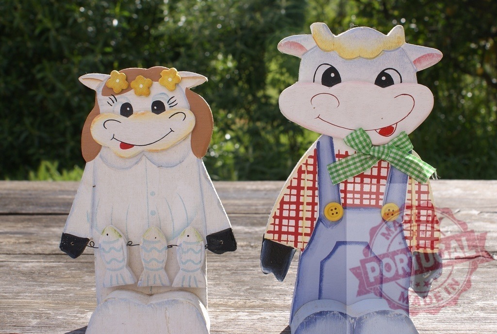 Wooden cow figurines representing a happy farmer couple | Wooden cow figurines dressed as a farmer couple on a rustic wooden table - Realized with Pictrs.com