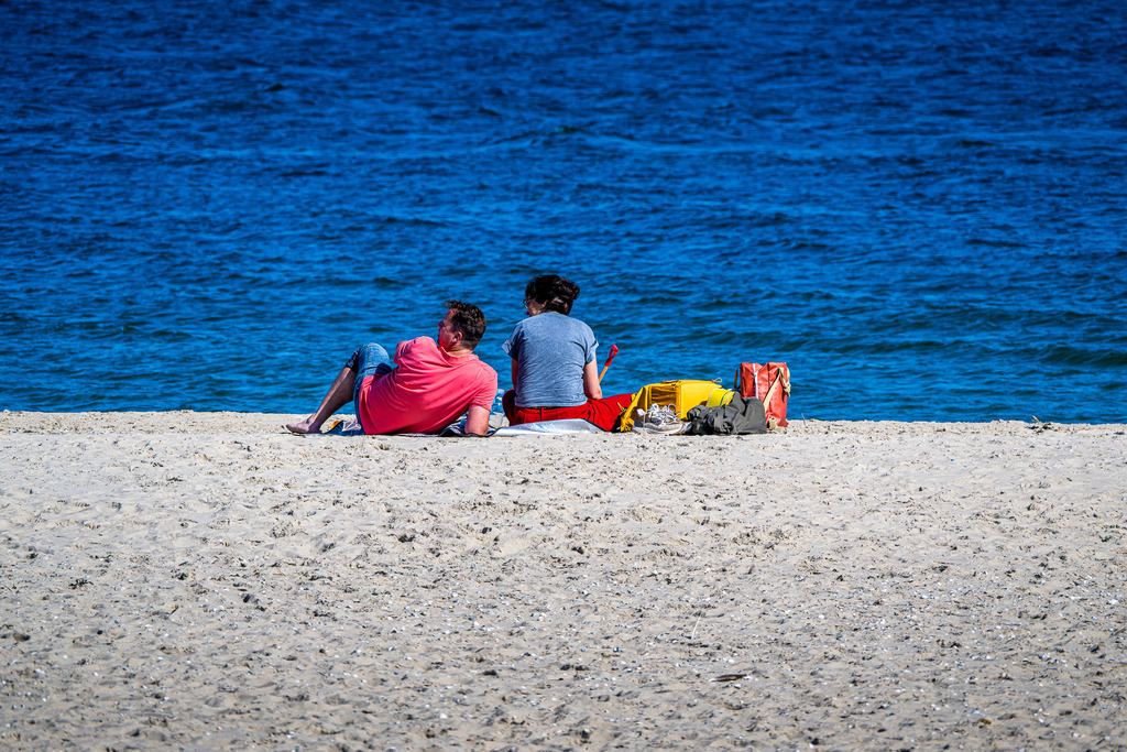 Spätsommerlicher Strandtag auf Texel: Paar genießt Auszeit an der Nordsee | Ein Paar sitzt entspannt im hellen Sand am Strand der holländischen Nordseeinsel Texel und blickt auf das tiefblaue Meer. Die ruhige Küstenatmosphäre fängt Momente von Erholung, Zweisamkeit und Urlaubsidylle ein. Mit leichtem Gepäck am Strand bietet die Szene ein stimmungsvolles Motiv für Themen wie Tourismus, Freizeit, Naherholung und Reisen an die niederländische Küste. - Realisiert mit Pictrs.com