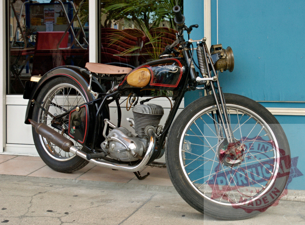 Vintage saroléa motorcycle parked near blue wall | Black vintage saroléa motorcycle parked on sidewalk near blue wall - Realized with Pictrs.com