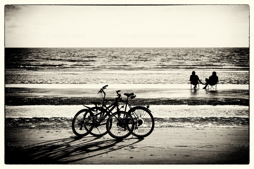 PFoArt_6577modnk2_180x120 | Weststrand. 2 Fahrräder stehen am Flutsaum. Ein Paar - Frau und Mann - sitzt auf 2 Stühlen auf einer Sandbank - vom Nordseewasser umspült.

Bildanmutung - Duoton. - Realisiert mit Pictrs.com
