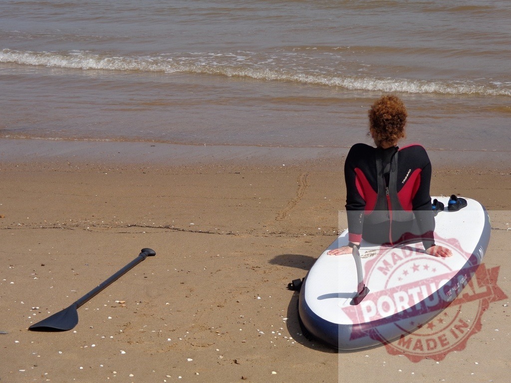Woman in wetsuit sitting on paddleboard watching ocean | Woman in wetsuit sitting on a paddleboard on the sand watching ocean waves - Realisiert mit Pictrs.com