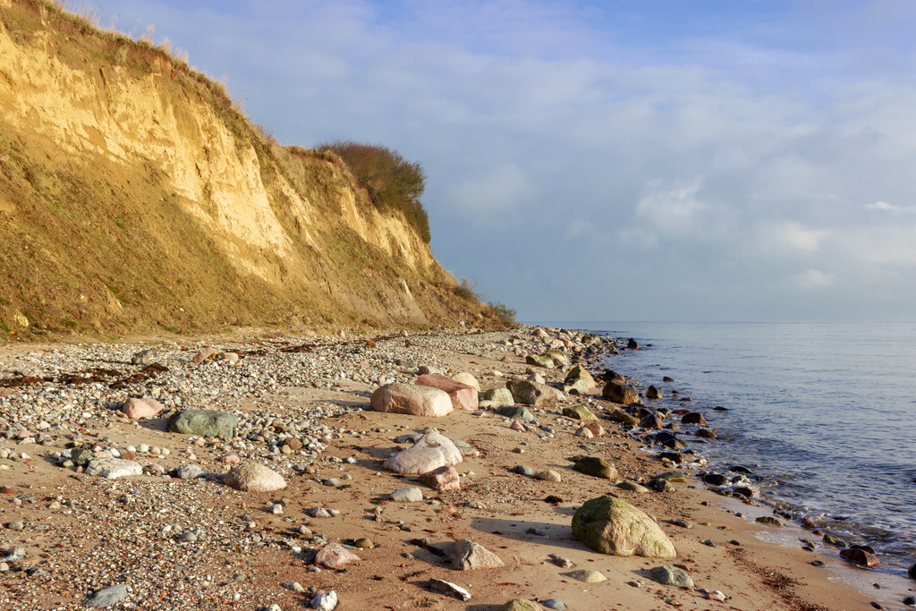 Wandbild: Steilküste in Kleinwaabs im Winter | Dieses Wandbild im Querformat zeigt die Steilküste in Kleinwaabs im Winter. Im Vordergrund ist der Naturstrand mit vielen großen Steinen zu sehen. Direkt dahinter befindet sich die Steilküste. Am Himmel sind viele Wolken zu sehen.  - Realisiert mit Pictrs.com