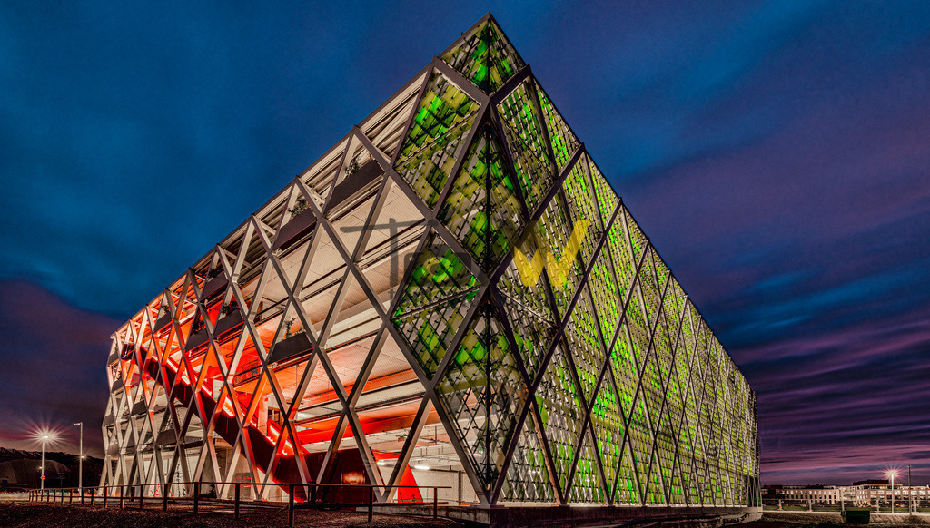 Das Quartiersparkhaus Q 16 in Stuttgart Bad Cannstatt--NEU | Das abgebildete Gebäude ist das Quartiersparkhaus Q16 mit integrierter Energiezentrale im NeckarPark in Stuttgart-Bad Cannstatt. BeschreibungStandort: Das Q16 befindet sich im neu erschlossenen NeckarPark in Bad Cannstatt.Funktion: Es dient als Parkhaus für das entstehende Quartier und gleichzeitig als nachhaltige Energiezentrale. Es kombiniert somit Parkmöglichkeiten mit der Energieversorgung für das umliegende Gebiet.Architektur: Das Gebäude ist für seine moderne und auffällige Architektur bekannt, entworfen von asp Architekten. Die Fassade zeichnet sich durch eine gläserne Schuppenhaut und eine Wabenstruktur aus, die sowohl Schalldämmung als auch natürliche Belüftung ermöglicht.  - Realisiert mit Pictrs.com