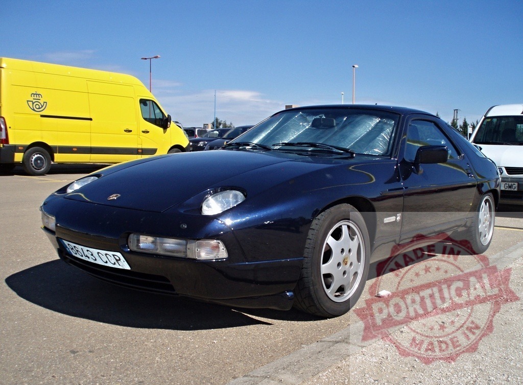 Dark blue Porsche 928 S4 parked in parking lot with sunshade on windshield | Porsche 928 S4 parked in a parking lot on a sunny day, with a sunshade protecting the interior - Realisiert mit Pictrs.com