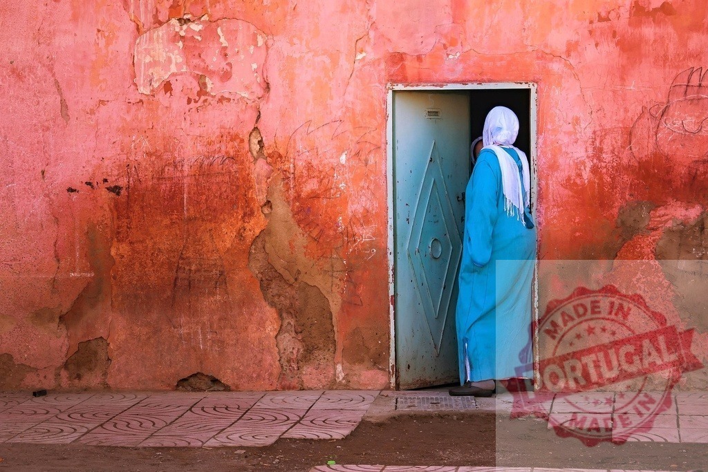Woman entering doorway in traditional Moroccan street | Woman in a blue dress and white hijab entering an old door against a textured red wall - Realized with Pictrs.com