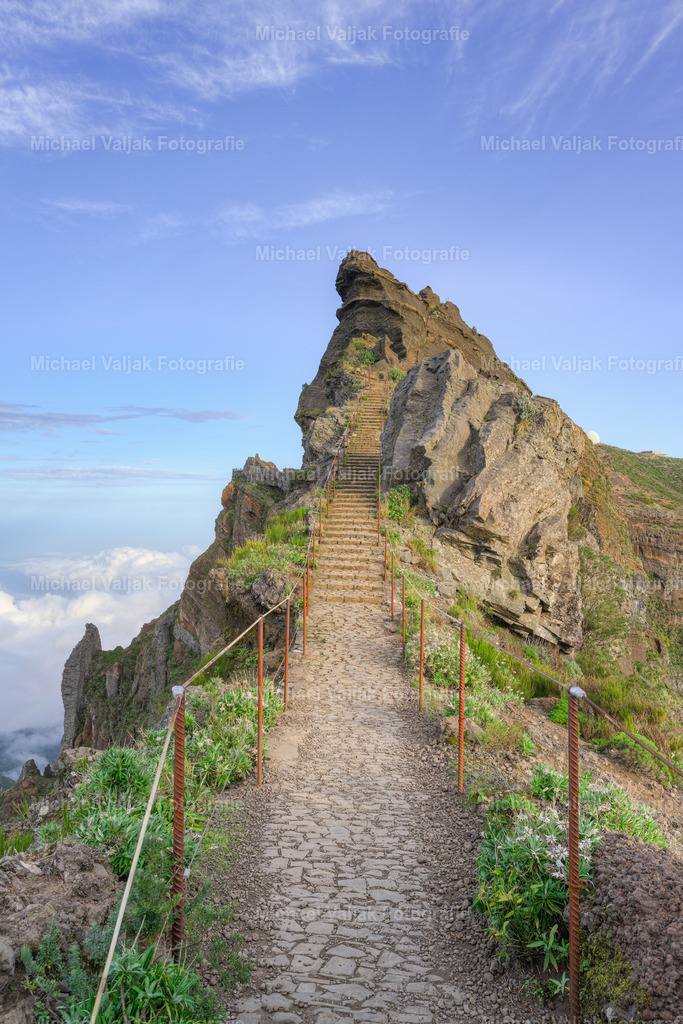 Himmelstreppe auf Madeira | Die Himmelstreppe in der Nähe des Pico do Arieiro auf Madeira ist eine steile Treppe, die sich entlang des Bergrückens emporwindet. Umgeben von schroffen, felsigen Gipfeln und karger Vegetation, führt die Treppe hinauf in eine weite, sonnendurchflutete Landschaft. Die klare Luft ermöglicht einen beeindruckenden Blick auf die umliegenden Berge und Täler, die von grünen Wäldern und zerklüfteten Felsen geprägt sind. Das Spiel von sanftem Licht und Schatten auf den Stufen und der Landschaft betont die dramatische Erhabenheit der Szenerie. Die „Himmelstreppe“ wirkt auf diesem Bild wie ein natürlicher Pfad, der den Wanderer zu neuen Höhen führt, inmitten der beeindruckenden Natur Madeiras. - Realisiert mit Pictrs.com