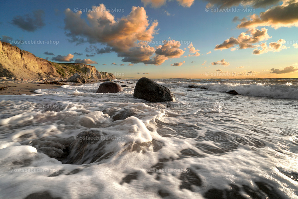 Goldene Stunde an der Steilküste | Große Steine und Findlinge versinken in den Wellen vorm Strand. Die Sonne zur goldenen Stunde taucht die Küste in ein warmes Abendlicht.