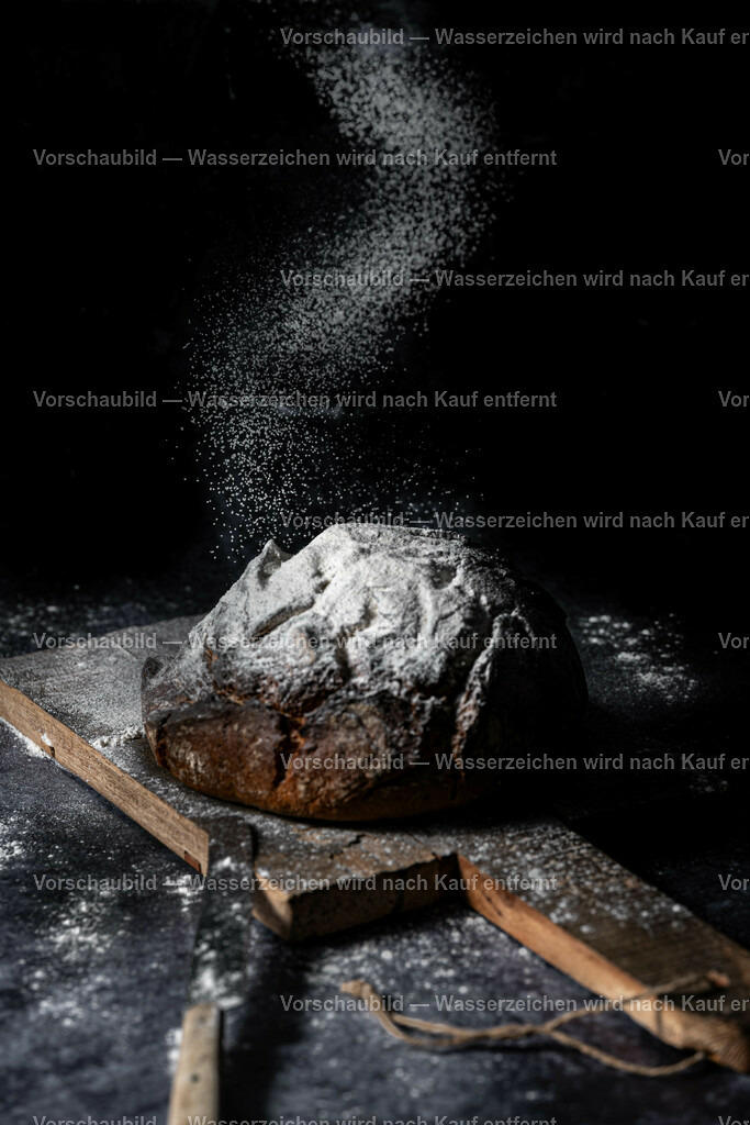 rustikales Bauernbrot wird mit Mehl bestöubt | rustikales Bauernbrot wird mit Mehl bestöubt, auf schneidenrett miut messer vor schwarzen Hintergrund - Realisiert mit Pictrs.com