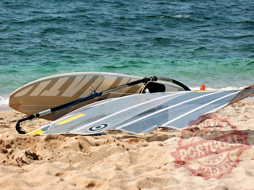Windsurfing equipment lying on sandy beach near the sea | Windsurf board and sail lying on the sand of a beach, suggesting recent activity - Realisiert mit Pictrs.com