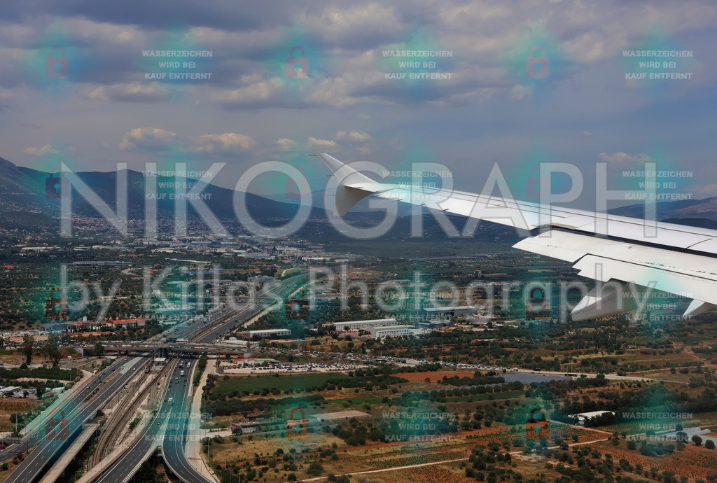 Flügel über Griechenland – Landeanflug mit Blick auf Hügel und Autobahnen | Blick aus dem Flugzeugfenster während des Landeanflugs – das weiße Flugzeugflügelende rahmt die Szenerie rechts ein und verleiht dem Bild Tiefe und Perspektive. Unterhalb erstreckt sich die Landschaft nördlich von Athen, im Raum Attika: mehrspurige Autobahnen schlängeln sich durch Olivenhaine und landwirtschaftliche Flächen, dazwischen moderne Industriegebäude, Parkplätze und Siedlungen. Im Hintergrund erheben sich die bewaldeten Hügel des Parnes-Gebirges unter einem leicht bewölkten Himmel. Die Szene vermittelt den Übergang zwischen Reise und Ankunft – zwischen Himmel und Erde, Natur und Infrastruktur.Ein authentischer „Window Seat“-Moment – der Flügel als visueller Anker, die Landschaft als dynamisches Mosaik aus Verkehr, Landwirtschaft und Siedlung. Die Farbpalette aus Erdtönen, Grün und Grau wirkt natürlich und dokumentarisch.Dieses Bild ist bei nikograph.eu erhältlich und kann als gerahmter Druck, Leinwandbild oder Poster in verschiedenen Formaten bestellt werden.