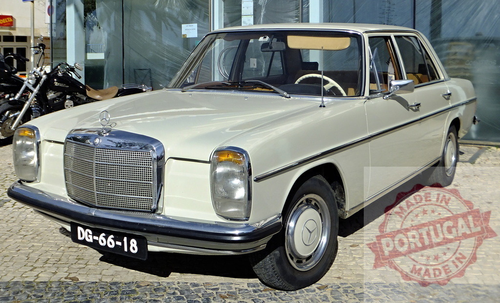 Mercedes-Benz w114 parked on cobblestone street reflecting in glass building | Classic white Mercedes-Benz w114 parked near glass building reflecting car and cobblestone street - Realisiert mit Pictrs.com