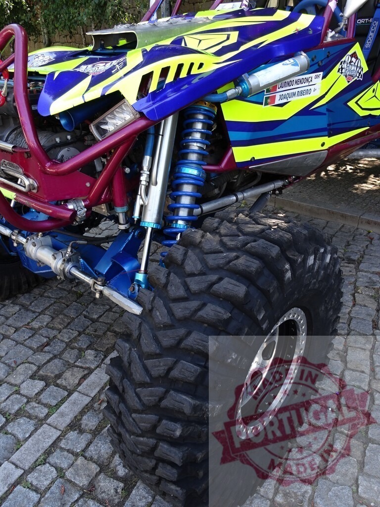 Buggy with big tires standing on cobblestone pavement | Close-up of a colorful buggy with large off-road tires parked on a cobblestone surface - Realized with Pictrs.com