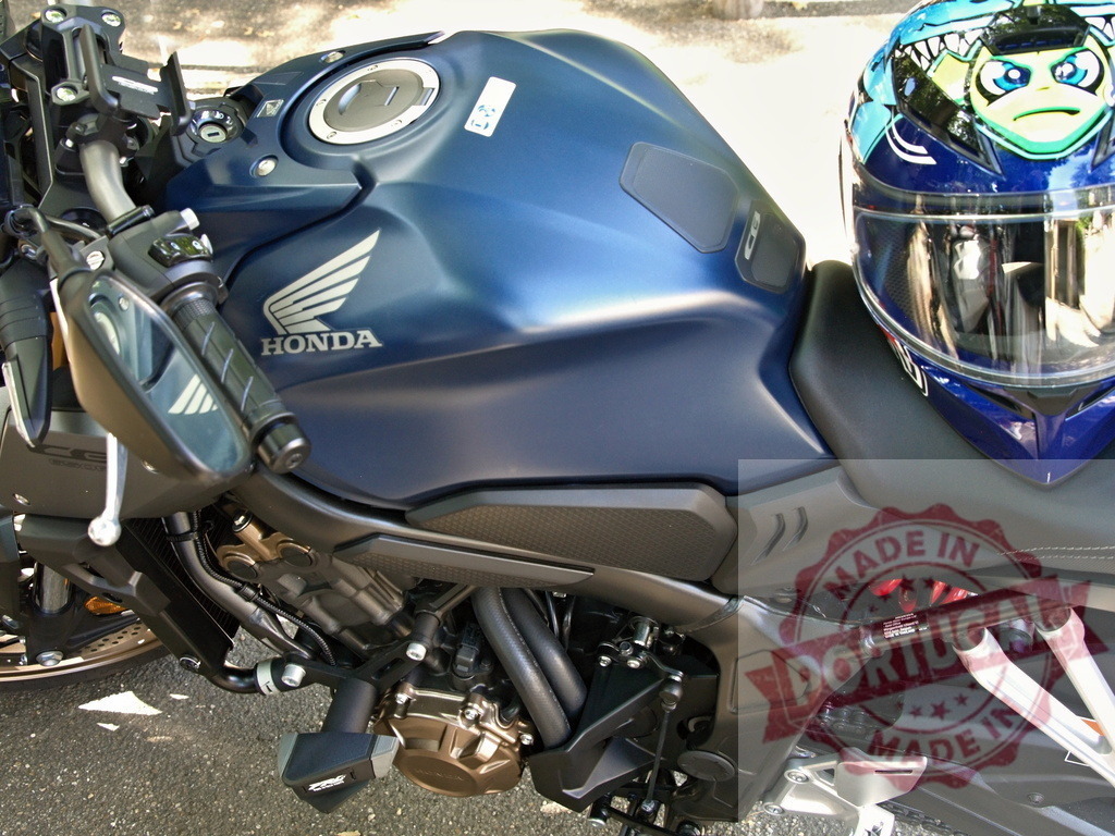 Close-up of Honda Motorcycle Tank with Helmet | Blue Honda motorcycle parked outdoors with a helmet resting on the seat - Realized with Pictrs.com