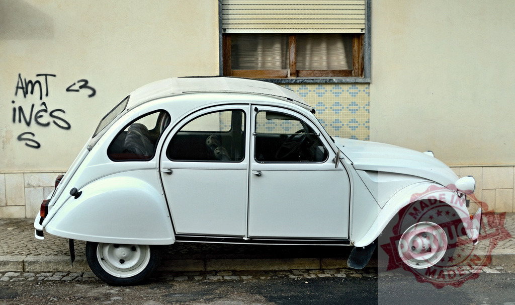 White Citroën 2CV parked near wall with graffiti | Classic white Citroën 2CV parked on the street next to a wall with graffiti - Realized with Pictrs.com