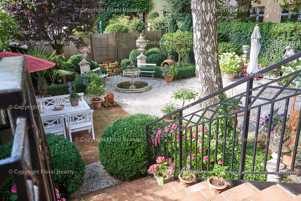 Mediterraner Stadtgarten | Städtischer Garten mit Treppenaufgang zum Balkon. Weiße Gartenmöbel und Tonstatuen und Brunnen. - Realisiert mit Pictrs.com